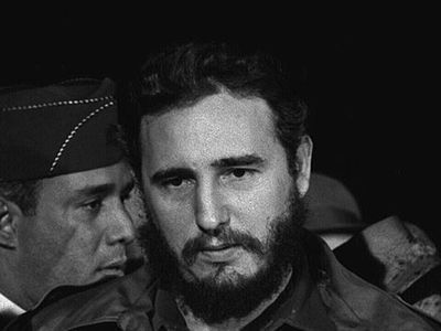 Young Fidel Castro stands in front of a bank of microphones.