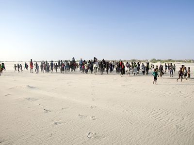  Dozens of people walk across a sandy lake bed on a sunny day.