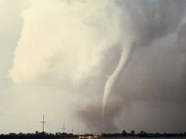 A photograph of a tornado as it touches down near a road.