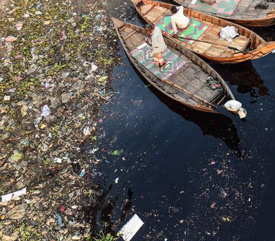 <p>Ferrymen wade their boats through the Buriganga river in Dhaka, Bangladesh, as plastic bags float by.</p>